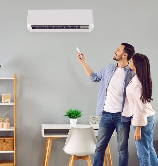 Young family couple using their modern air conditioning system at home. Happy husband and wife setting up the temperature on their white AC on the wall in the living room. Air conditioner concept